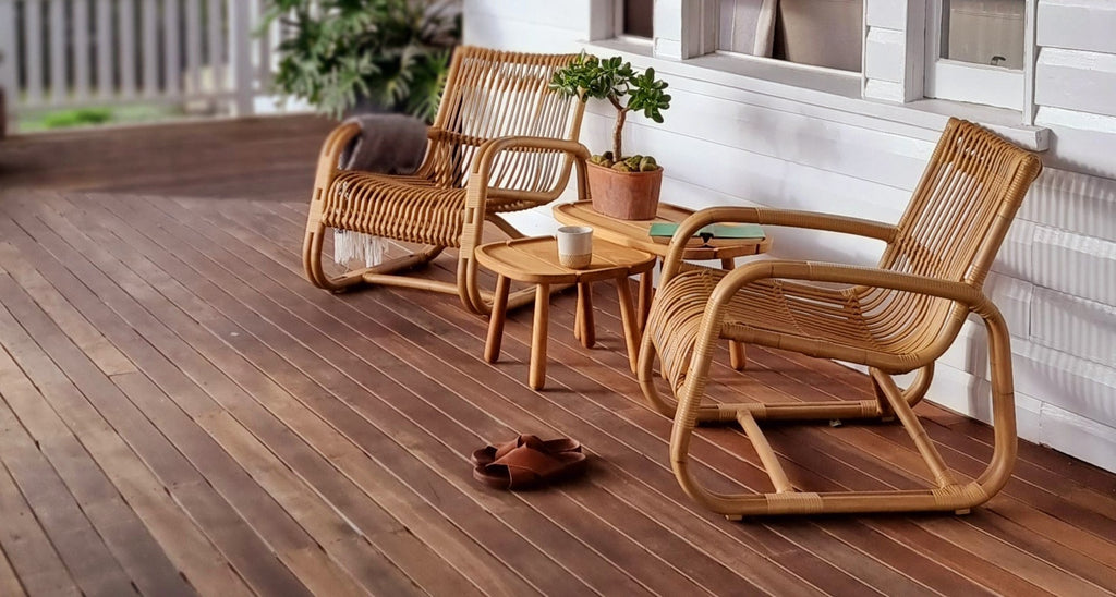Two nautral coloured lounge chairs on a veranda with teak side tables
