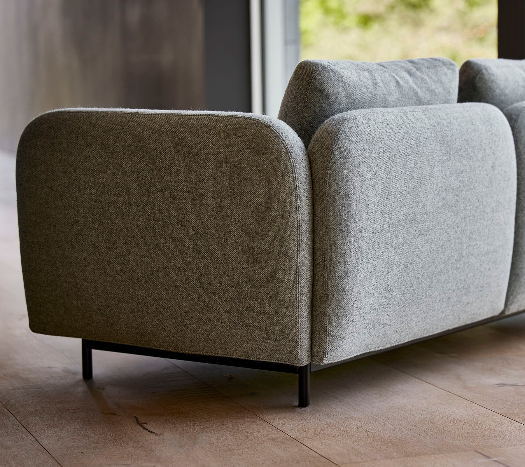 Ein modernes graues gepolstertes Sofa mit abgerundeten Kanten und schlanken schwarzen Beinen, das ein minimalistisches Design präsentiert.