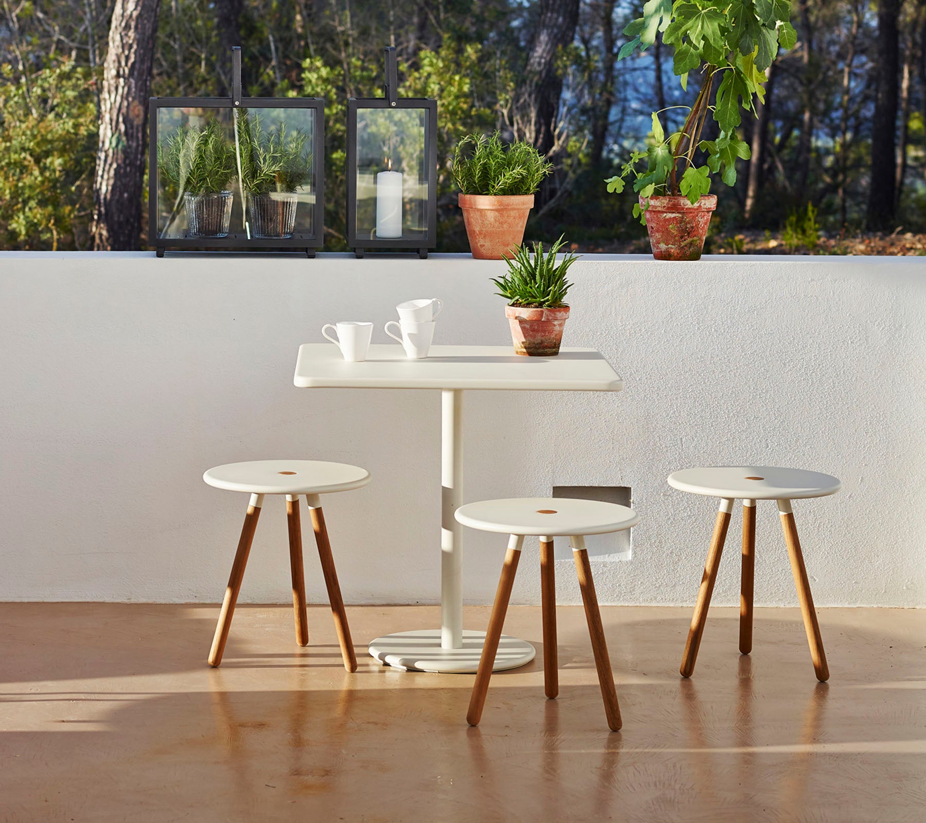 Ein minimalistischer Tisch mit drei passenden Hockern, umgeben von Topfpflanzen, die eine ruhige und einladende Atmosphäre schaffen.