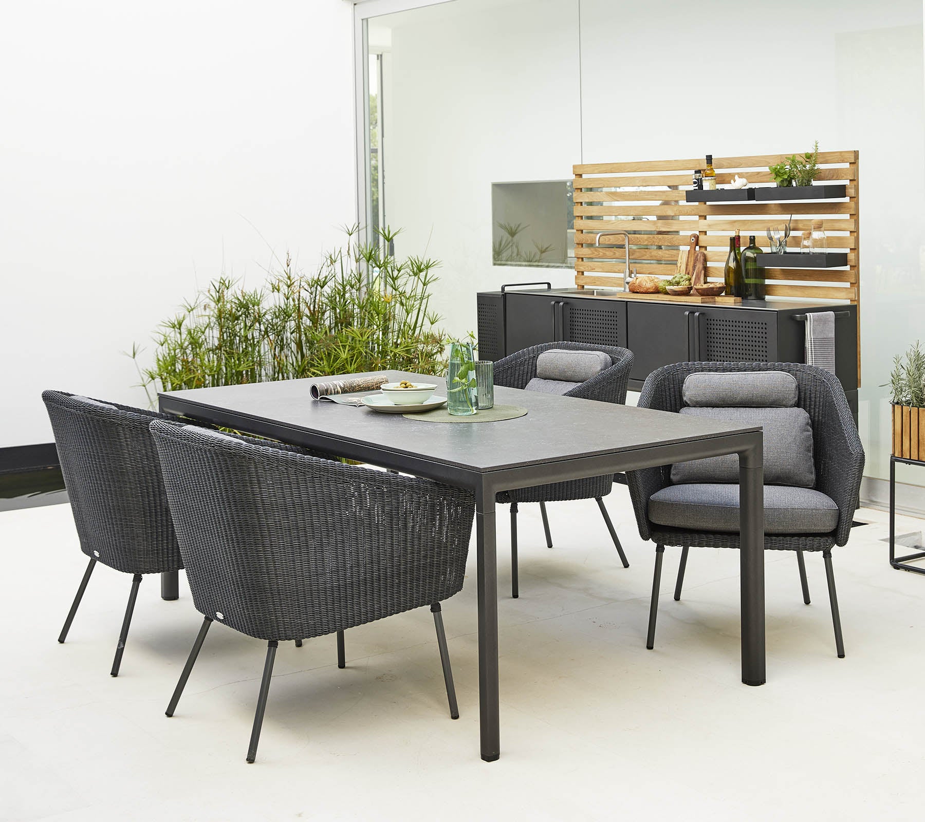 Stylisches Esszimmer-Set für den Außenbereich mit einem schlanken Tisch und bequemen, modernen Stühlen, umgeben von dekorativem Grün.