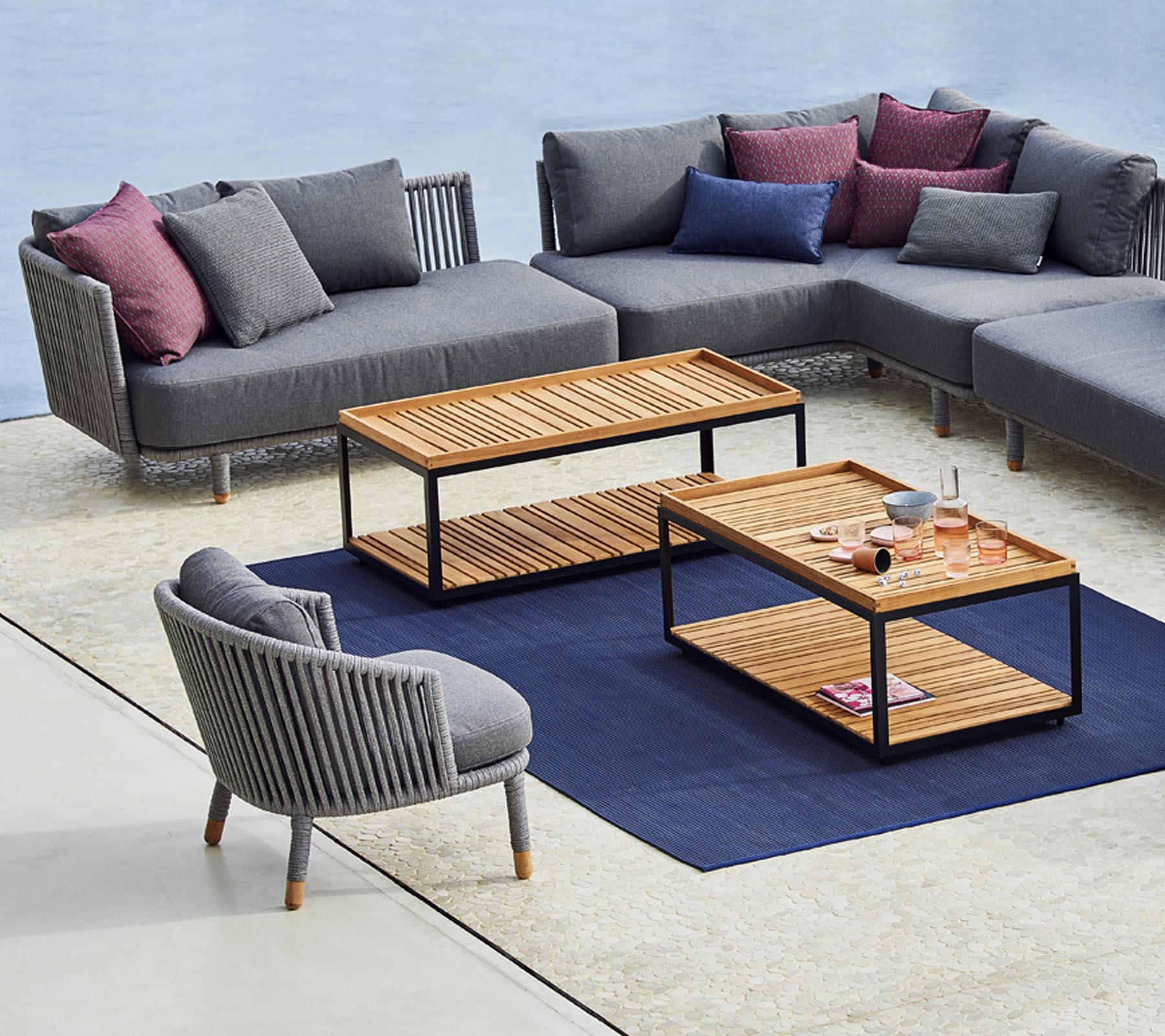 Moderne Sitzanordnung mit einem grauen Ecksofa, einem stilvollen runden Stuhl und Holztischen mit einem blauen Teppich darunter.