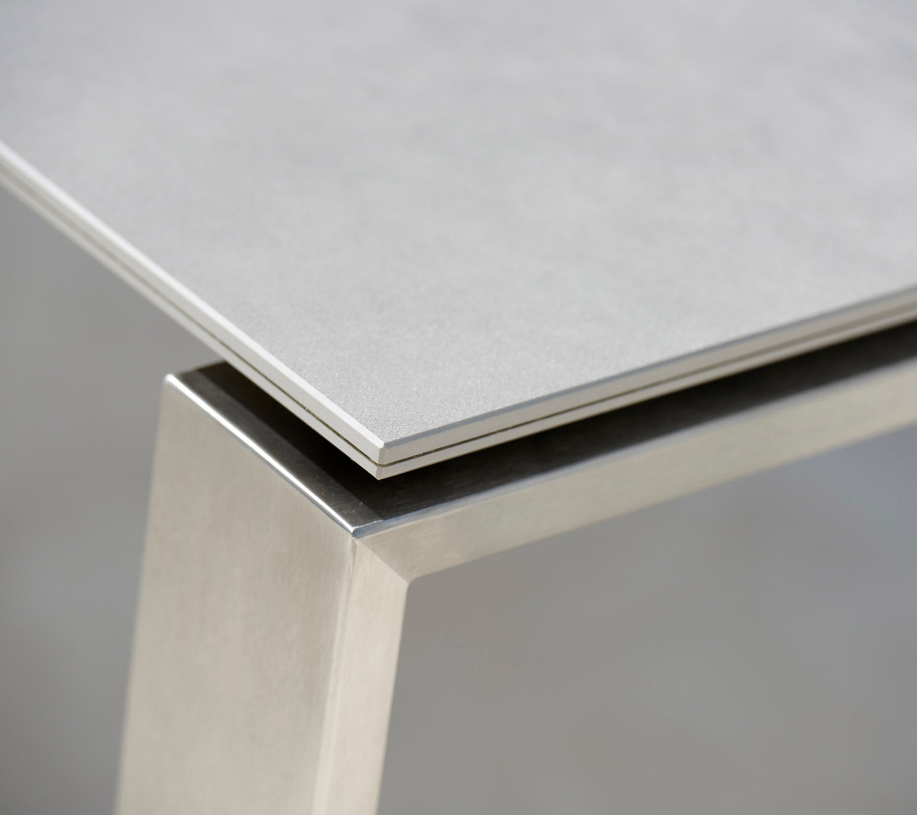 Nahaufnahme eines modernen Tisches mit einer eleganten grauen Oberfläche und einem Edelstahlgestell, das die kontrastierenden Materialien und die klaren Linien hervorhebt.