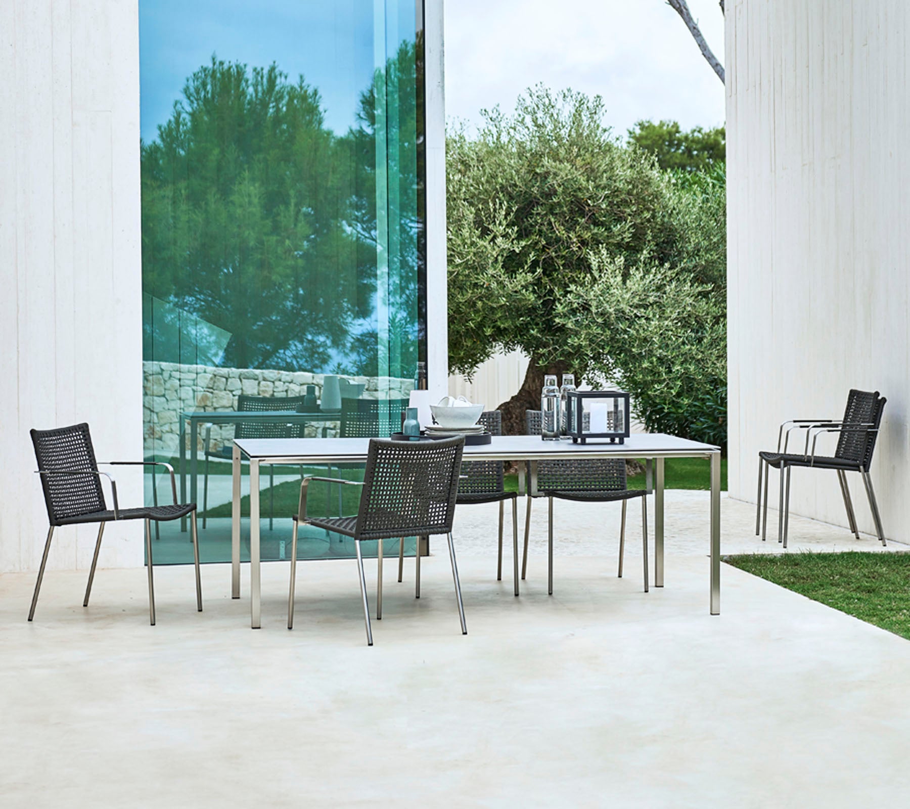 Ein modernes Outdoor-Essset mit einem rechteckigen Tisch und vier stilvollen Stühlen mit schlankem Design, umgeben von Grün.
