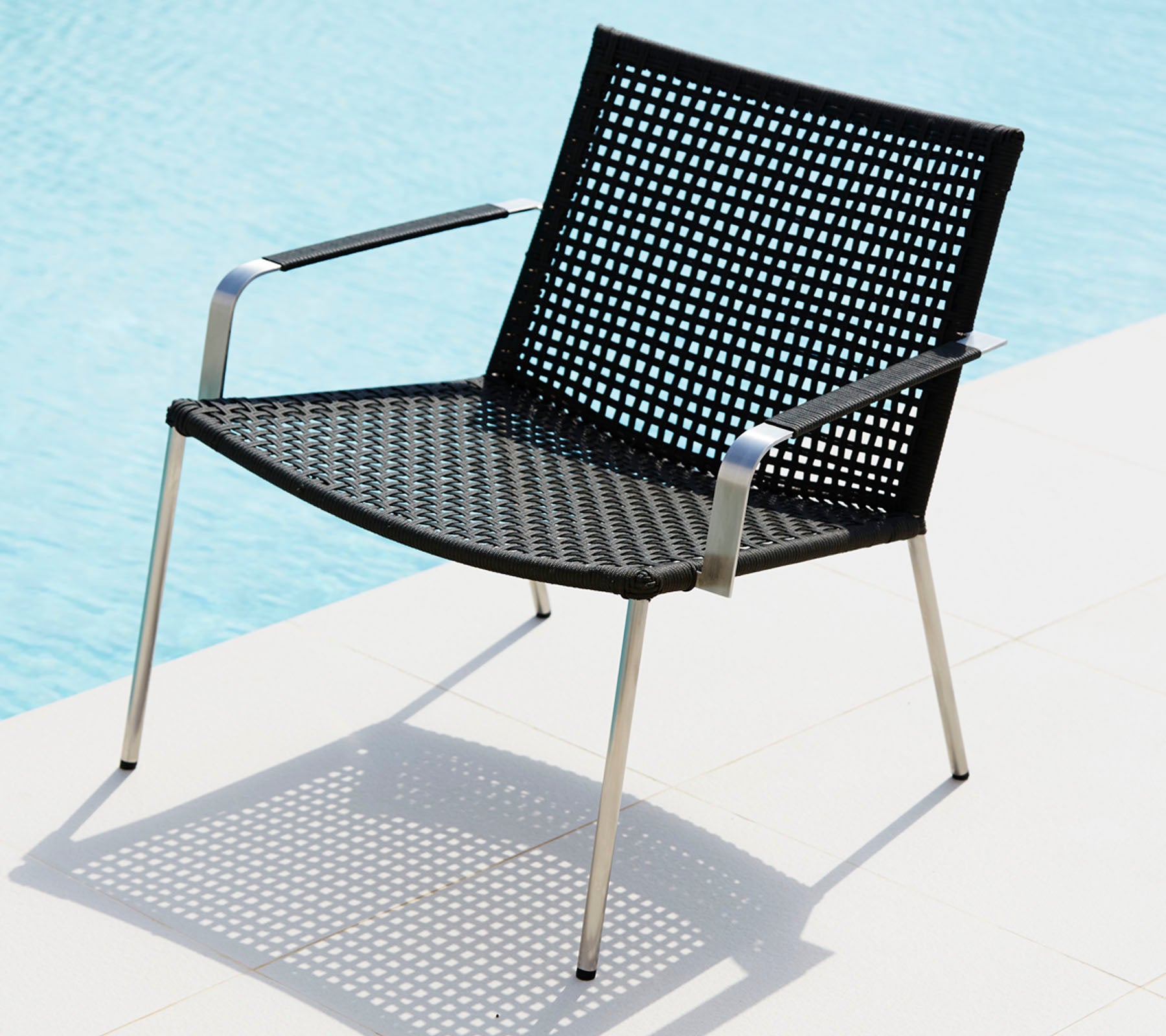 Stylischer schwarzer Stuhl mit einem durchbrochenen Design und schlanken Metallbeinen, der einen Schatten auf eine helle Oberfläche wirft.