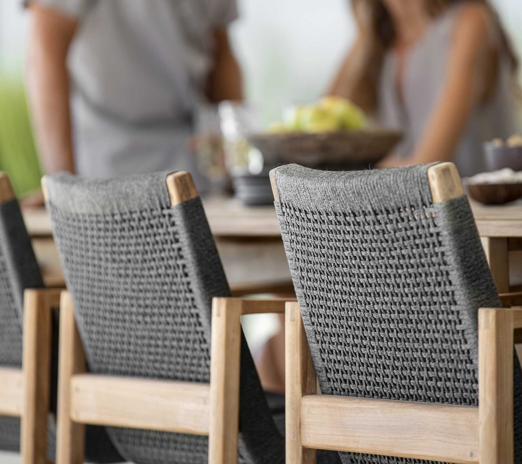 Außenspeiseszene mit einem Holztisch und zwei stilvollen grauen geflochtenen Stühlen, an dem Menschen gemeinsam eine Mahlzeit genießen.