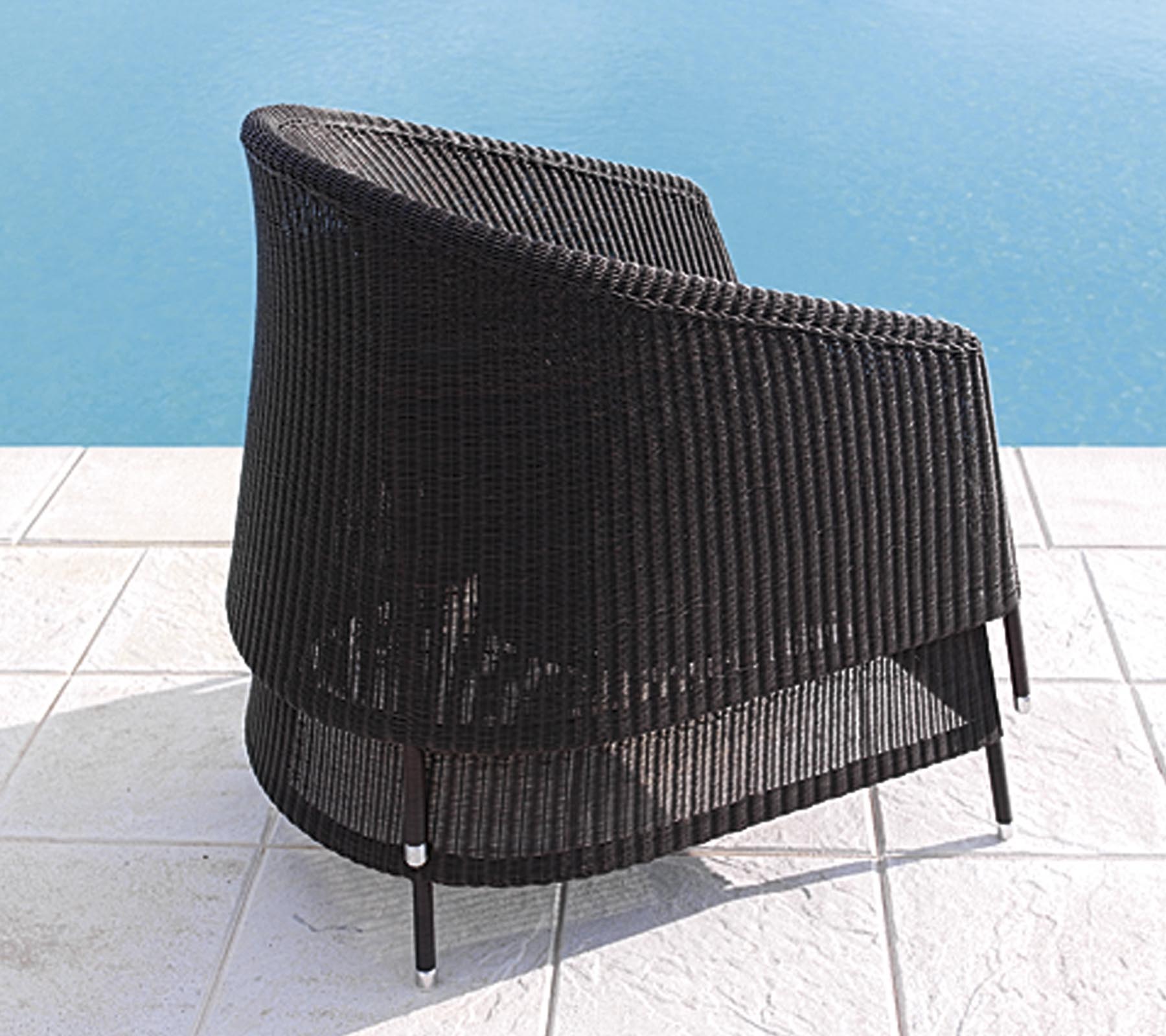 Abgeruhter schwarzer Rattanstuhl mit sleekem Design, positioniert in der Nähe eines Pools auf weiß gefliesten Böden.
