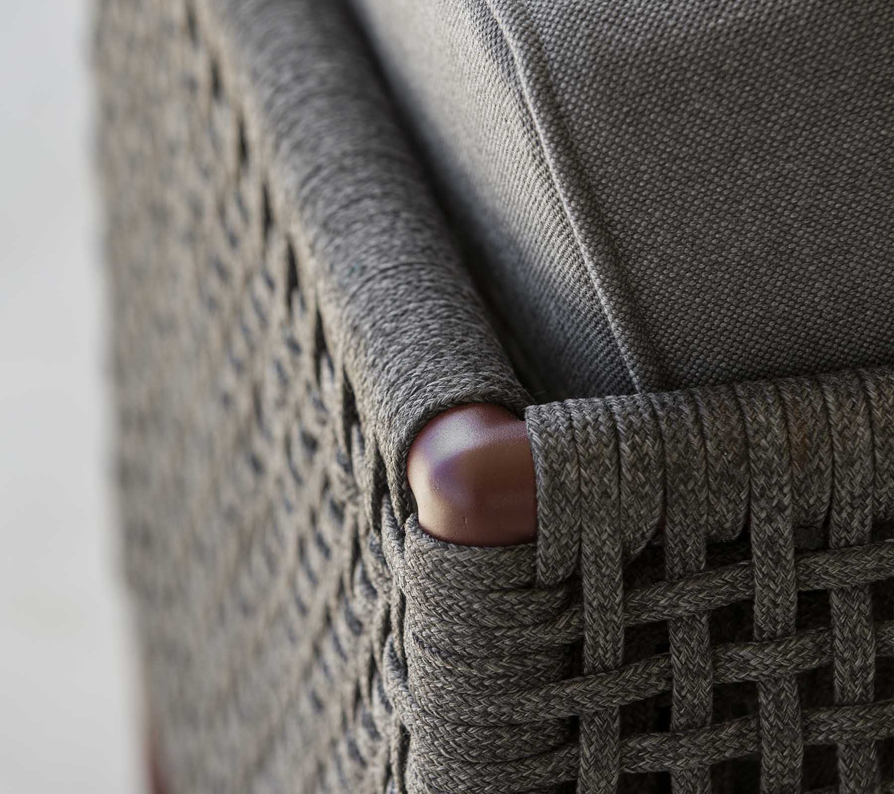 Eine Nahaufnahme einer geflochtenen Möbel-Ecke mit elegantem grauem Stoff und glatten Holzelementen, die eine Mischung aus Textur und Stil zeigt.