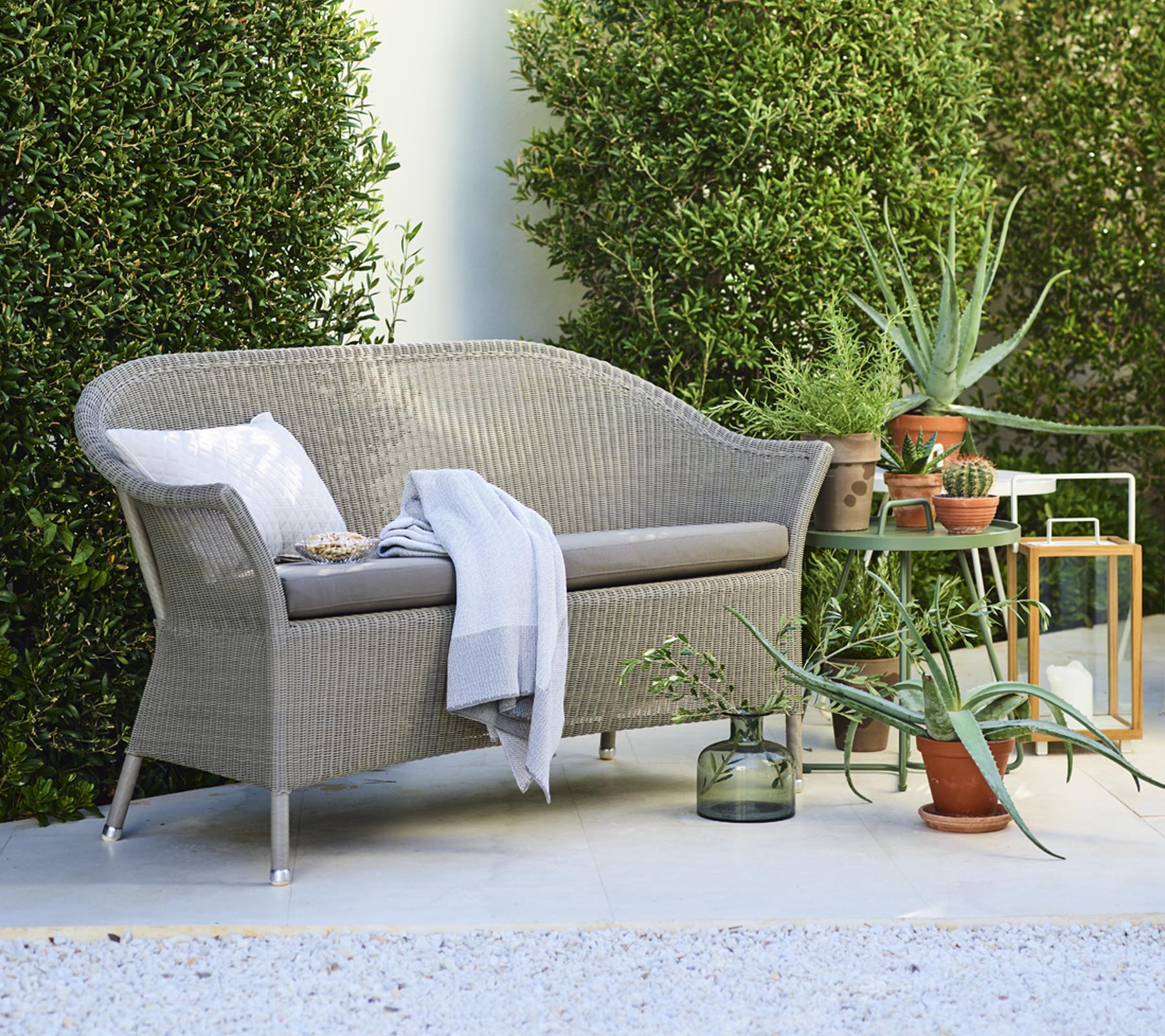 Ein gemütliches Loveseat mit dekorativen Kissen, begleitet von Topfpflanzen und einem Beistelltisch, umgeben von Grün.