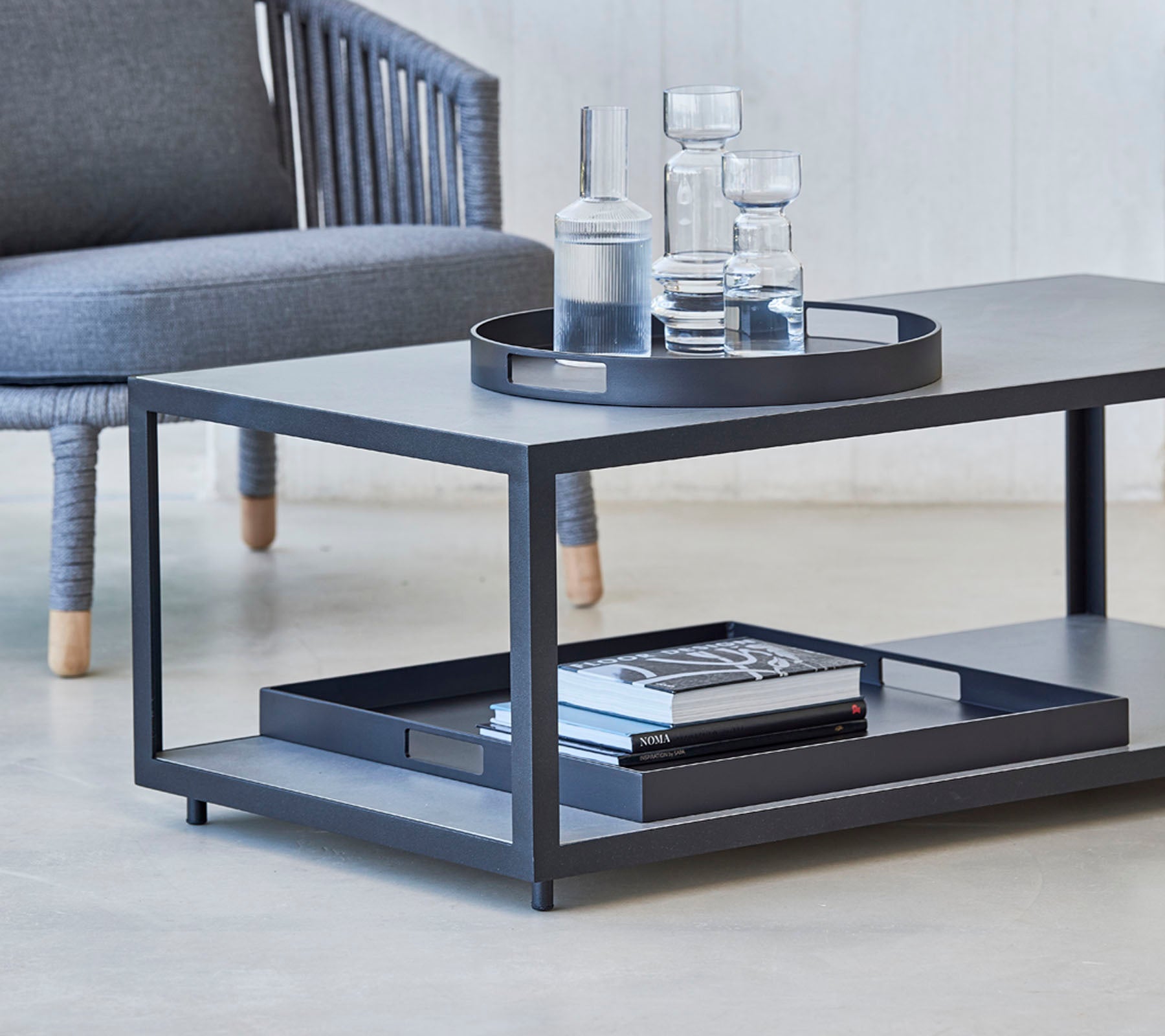 Modernes Couchtisch mit einem schlanken Design, mit einem Tablett, Gläsern und Büchern auf dem unteren Regal. Ideal für stilvolle Wohnräume.
