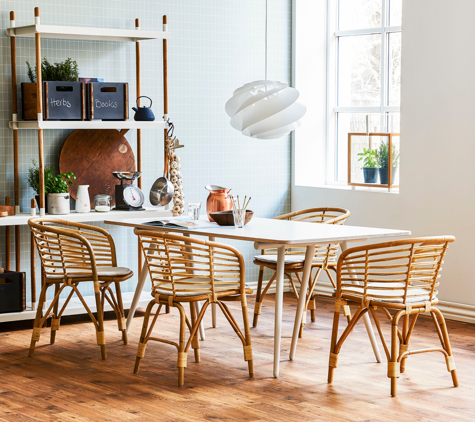Ein stilvoller Essbereich mit einem hellen Holztisch, umgeben von Rattanstühlen und einer modernen Pendelleuchte, ergänzt durch dekorative Regale.