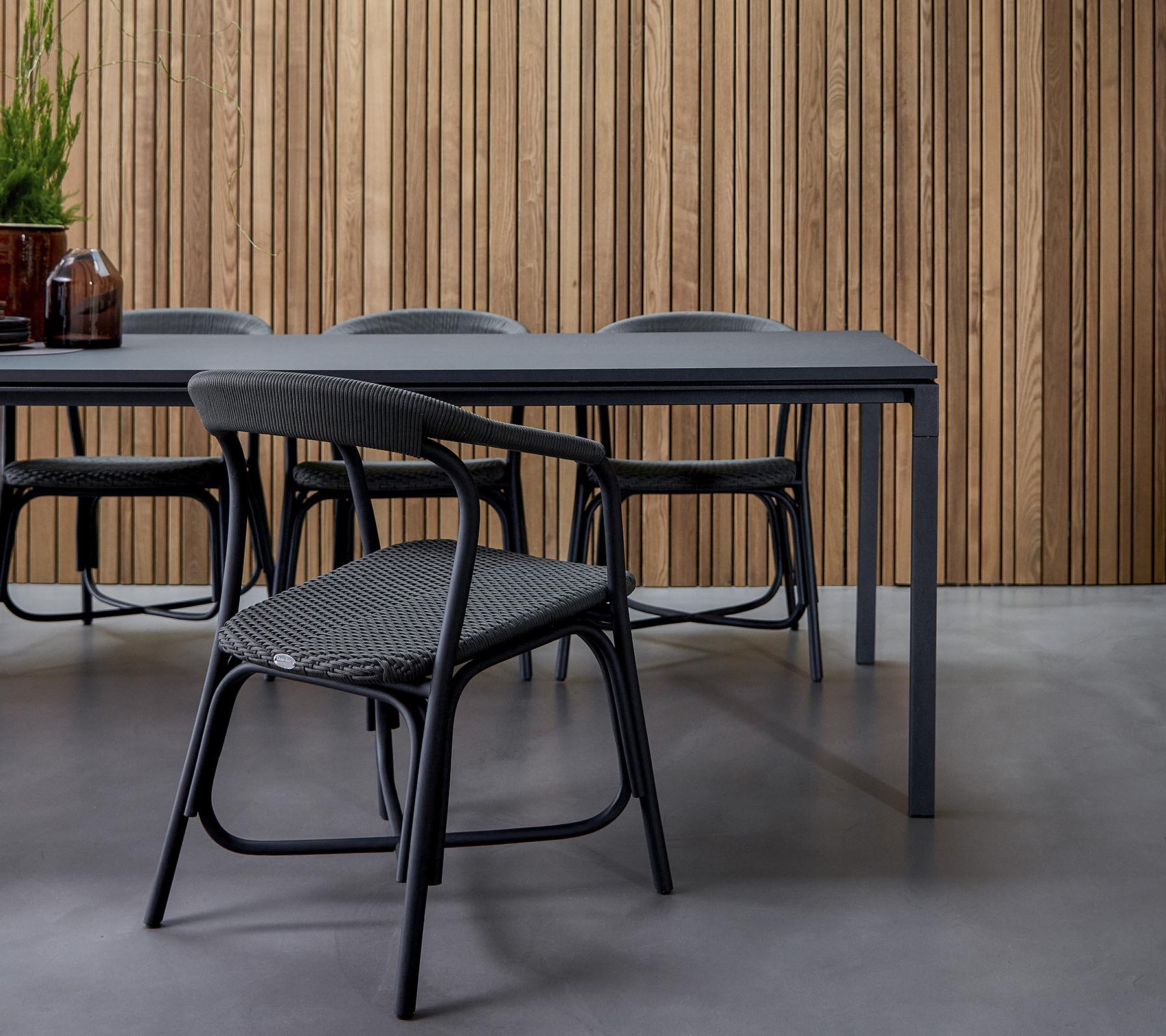 Ein modernes Essbereich mit einem eleganten Tisch, umgeben von stilvollen Stühlen, vor einem strukturierten Holz-Hintergrund.