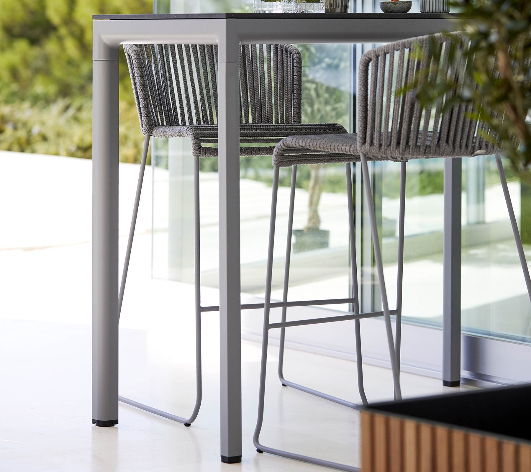 Ein eleganter, moderner Tisch mit passenden Hochlehnern, die ein minimalistisches Design und einen stilvollen Metallrahmen aufweisen, ergänzt durch natürliche Grünpflanzen.