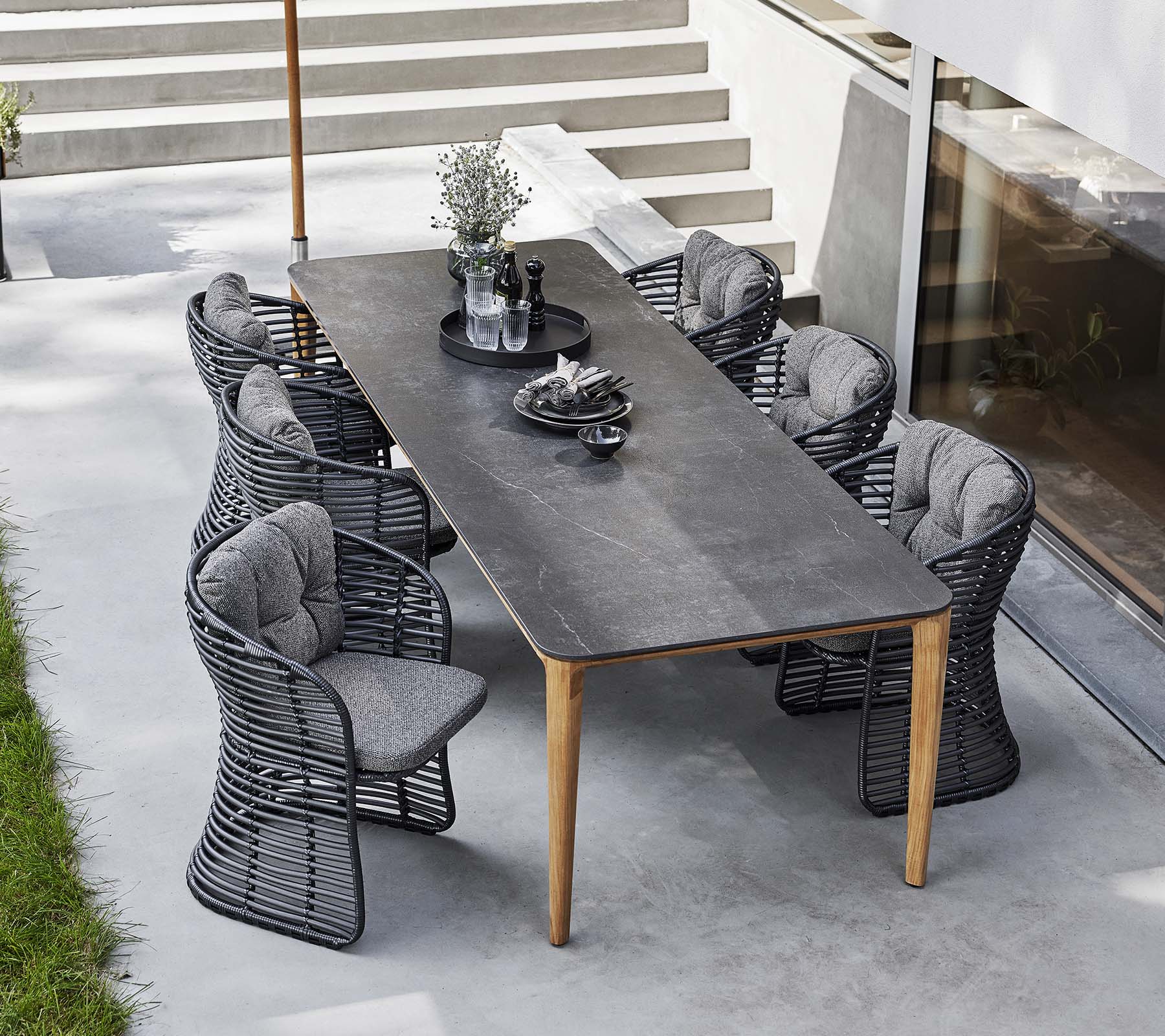 Korbsessel umgeben einen eleganten Tisch, ergänzt durch einen klassischen Sonnenschirm und dekorative Mittelstücke für ein einladendes Esssetup im Freien.