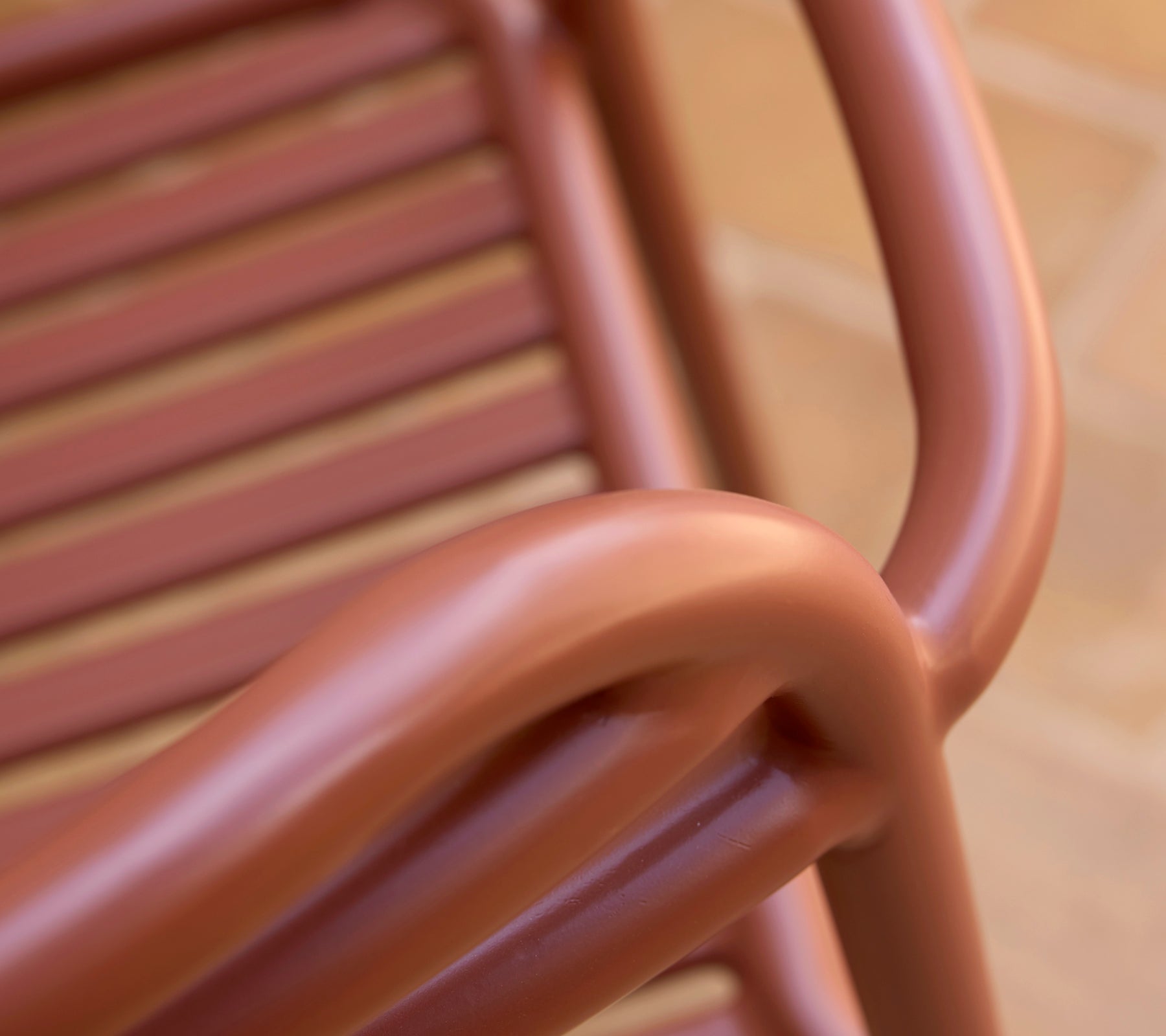 Nahaufnahme eines Bliss-Sessels in einem wüstenroten Farbton, der seine sanften Kurven und das Latten-Design zeigt.