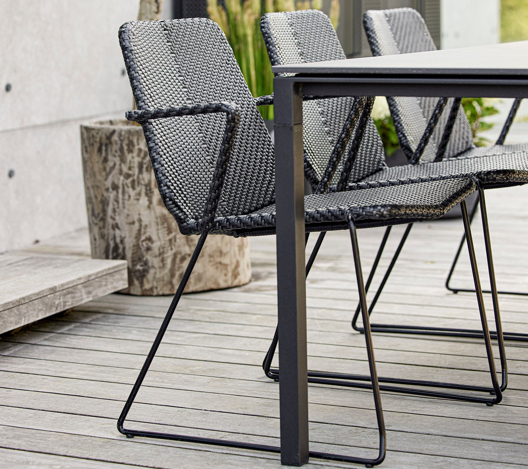 Ein Set moderner schwarzer geflochtener Stühle, die um einen eleganten Tisch angeordnet sind und zeitgemäßes Design und Handwerkskunst präsentieren.