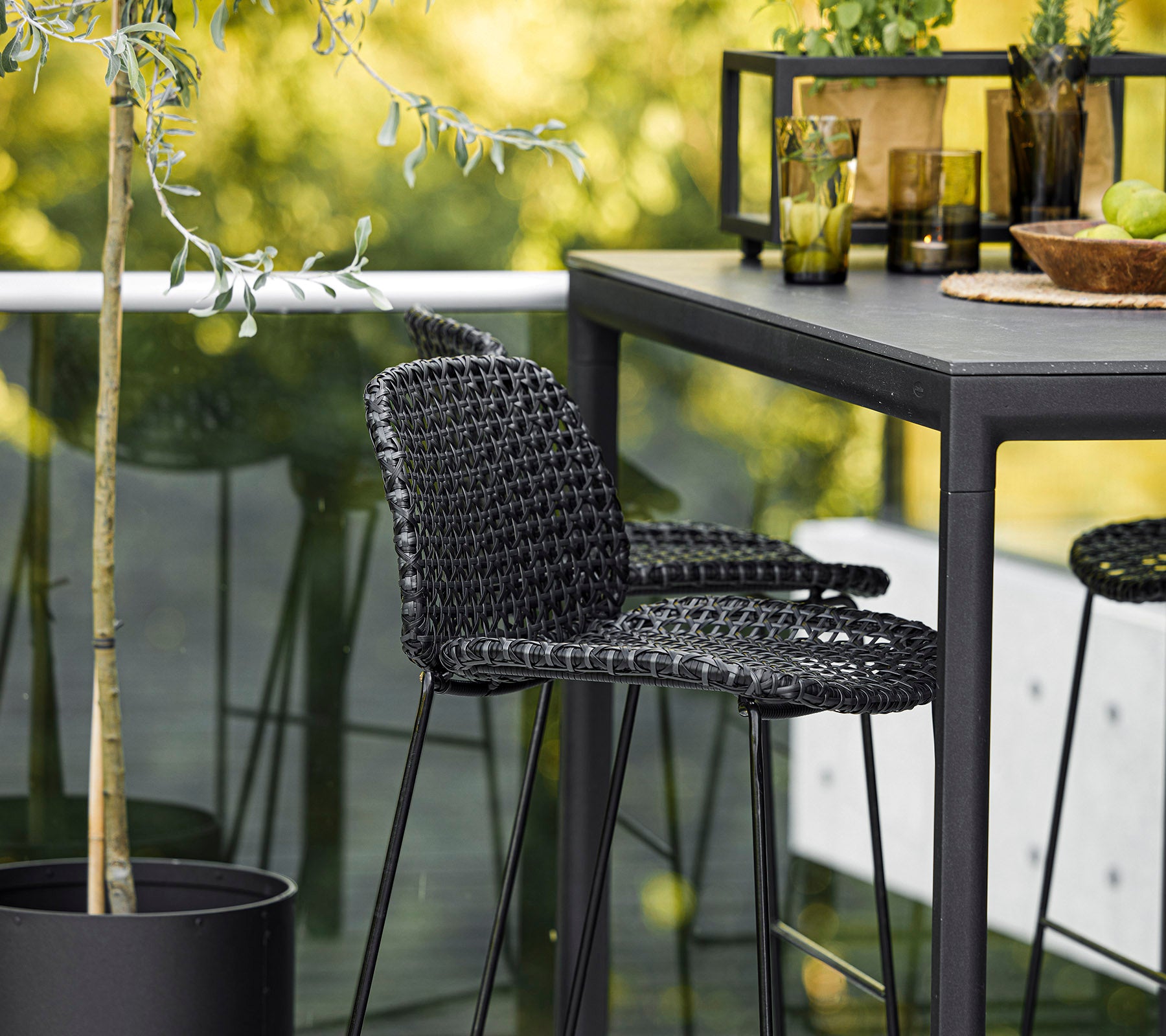 Ein stilvoller schwarzer geflochtener Stuhl kombiniert mit einem eleganten Tisch, umgeben von dekorativen Pflanzen und Glaswaren, schafft ein modernes Ambiente.