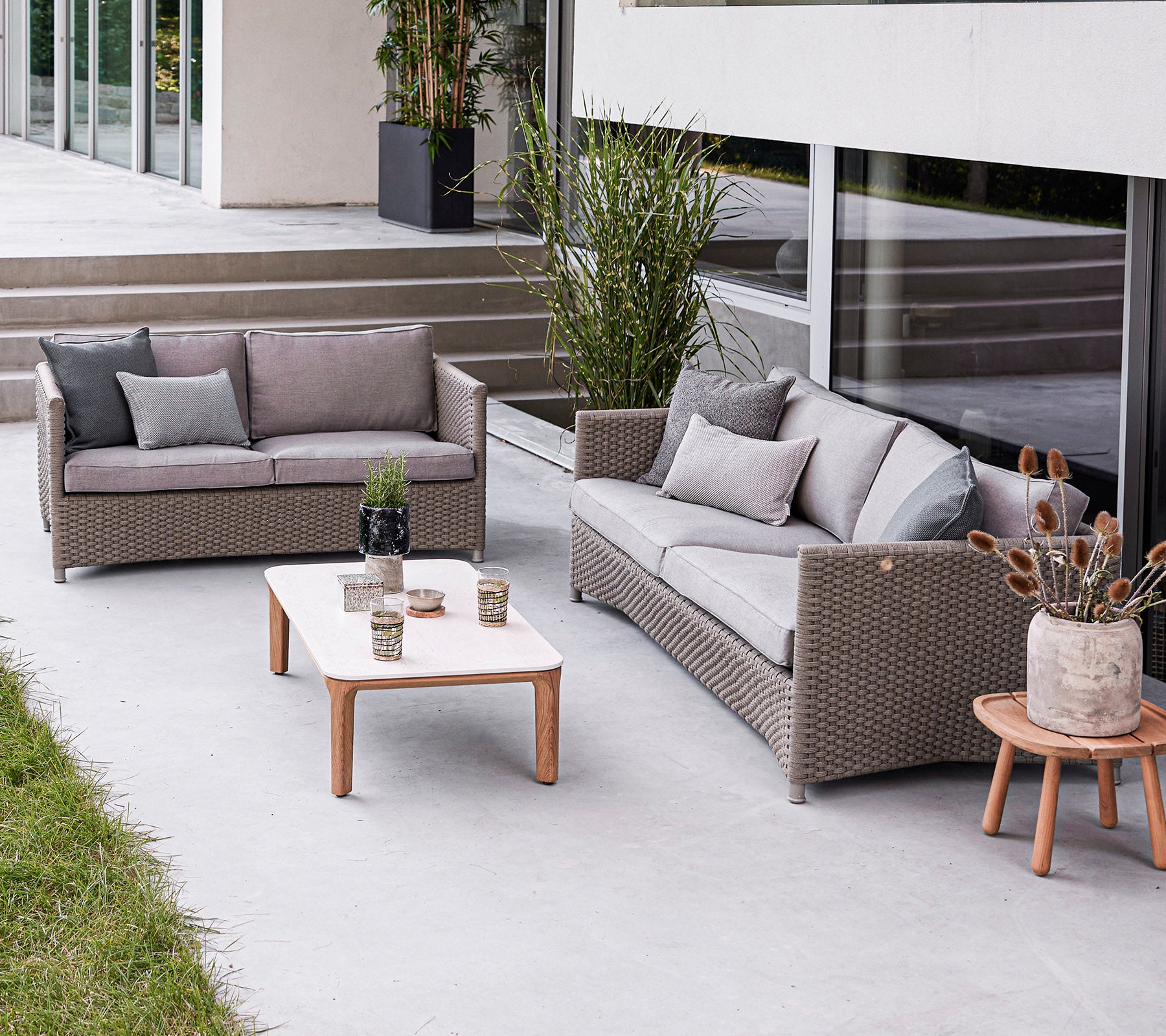Moderne Außen-Sitzbereich mit einem Sofa, einem Loveseat und einem Couchtisch mit dekorativen Elementen. Stilvolle und einladende Atmosphäre.
