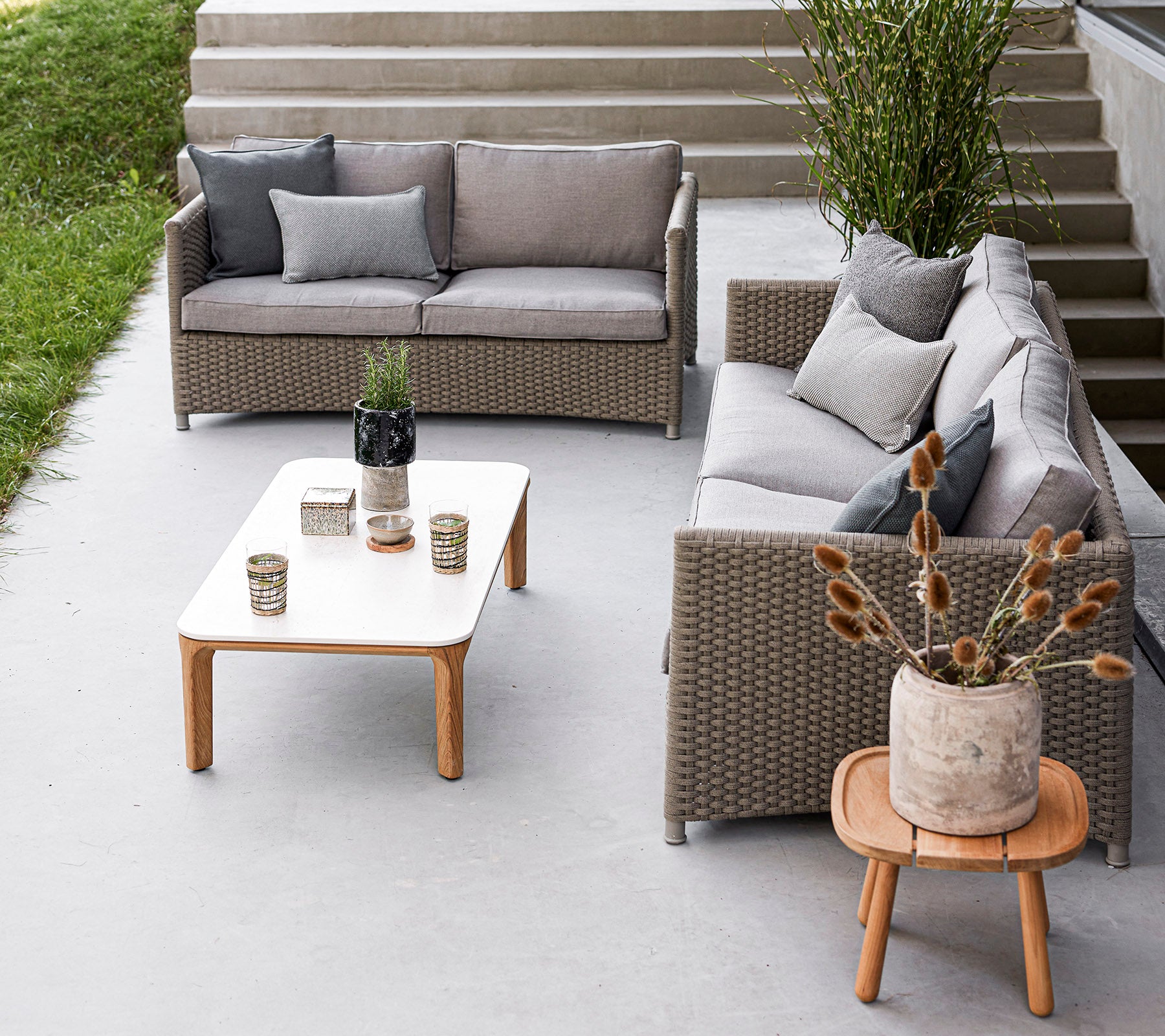 Stylische Sitzgelegenheit im Freien mit einem grauen Sofaset, einem Holztisch, dekorativen Vasen und Topfpflanzen. Ideal zur Entspannung.