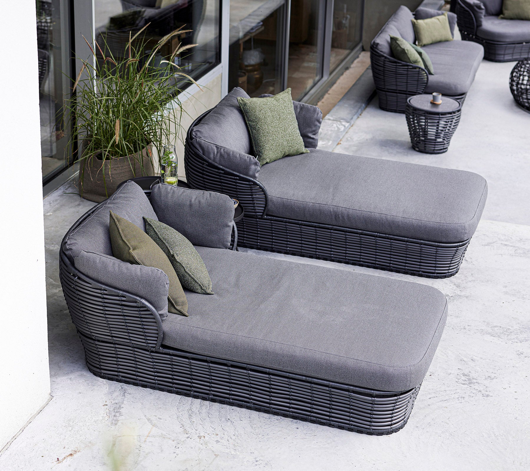 Zwei moderne Loungestühle mit plüschigen grauen Kissen und grünen Akzentkissen, begleitet von einem runden Beistelltisch.
