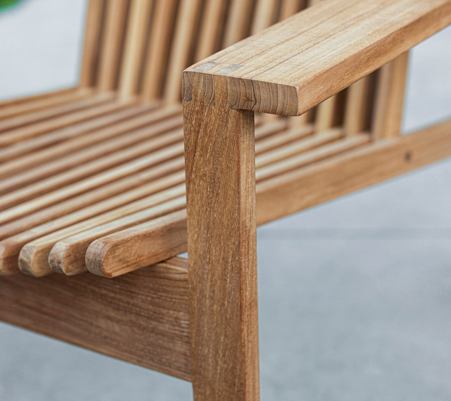 Nahaufnahme einer Holzbank mit lattenartigem Design und einer stabilen Armlehne, die die natürliche Holzmaserung und Handwerkskunst zeigt.
