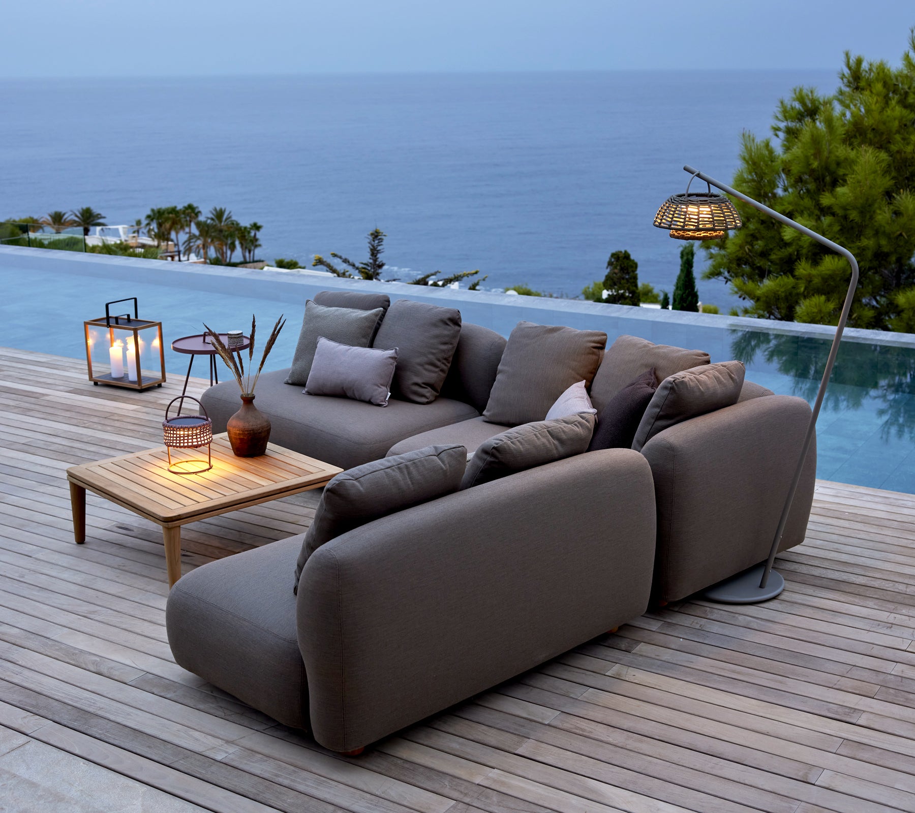 Grau Sofa mit Holztisch und Laternen am Pool mit Blick auf den Ozean.