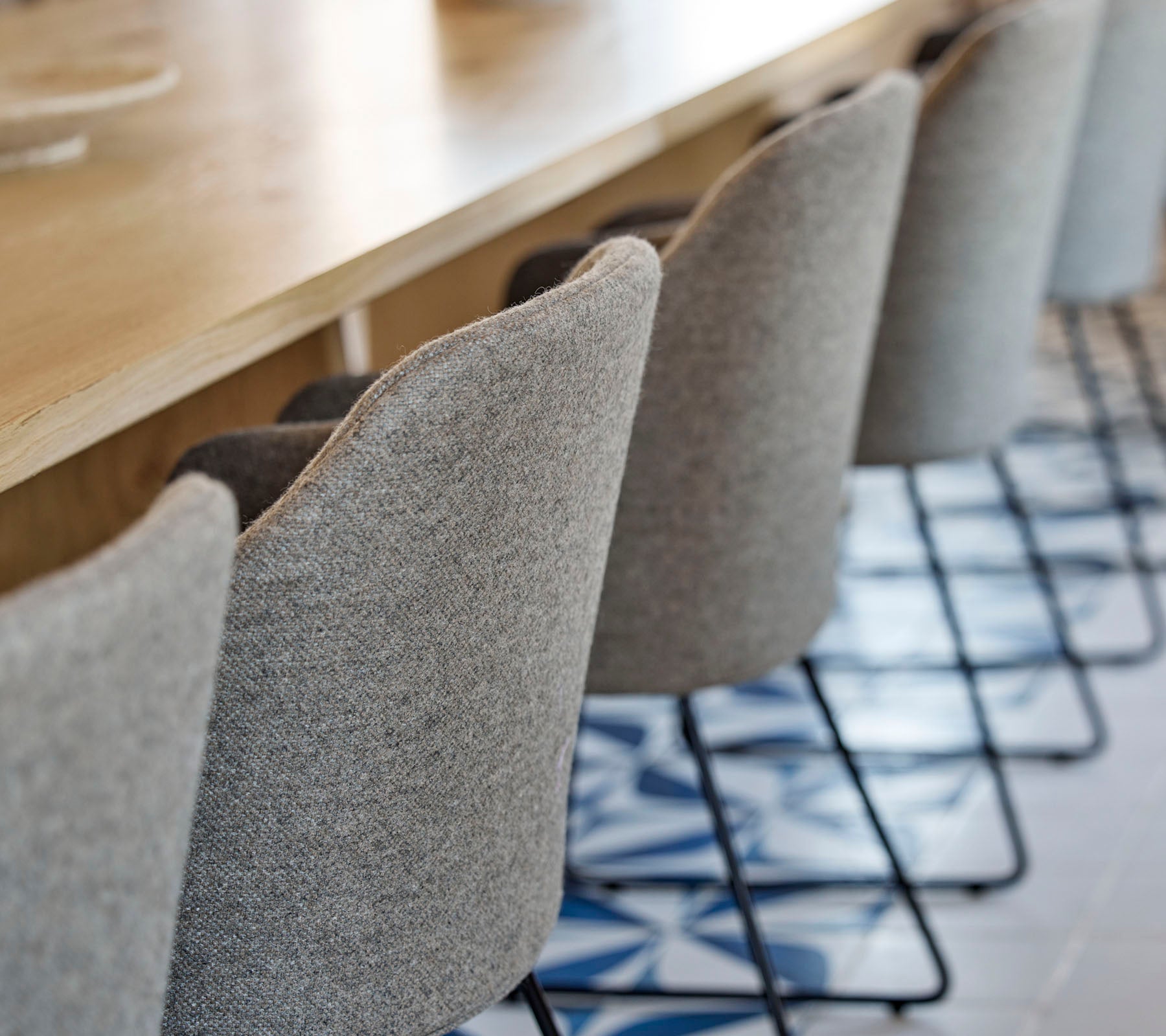 Eine Reihe stilvoller, gepolsterter Stühle mit schlanken Metallbeinen, die um einen Holztisch angeordnet sind, mit gemustertem Boden darunter.