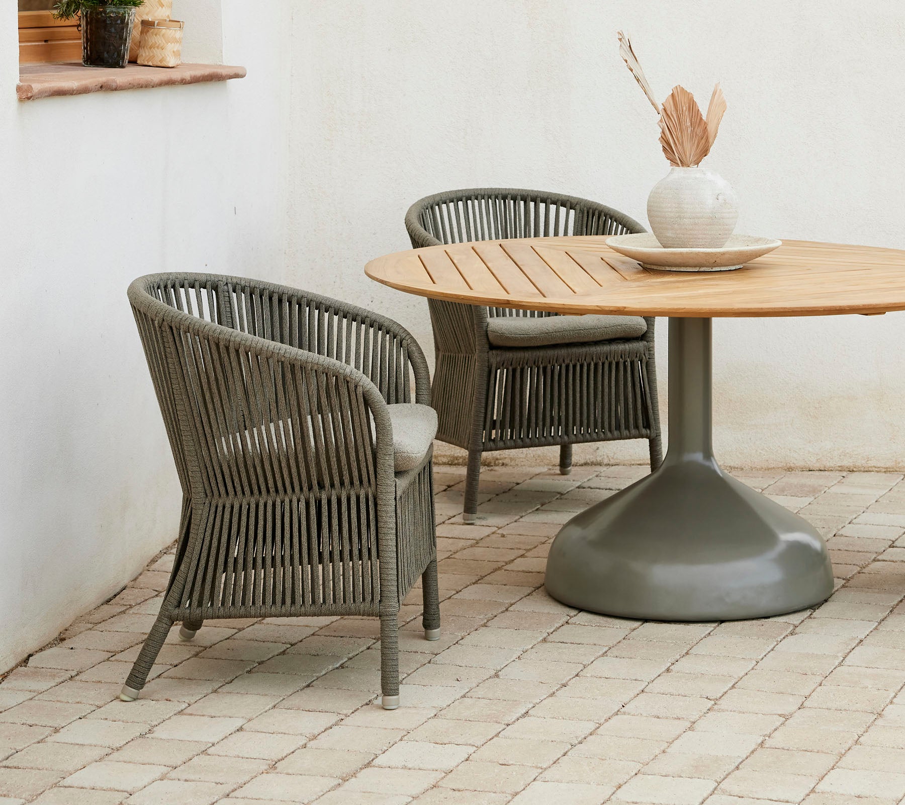 Zwei stilvolle Derby-Stühle kombiniert mit einem runden Glaze-Esstisch, der eine neutrale Farbpalette und eine dekorative Vase präsentiert.