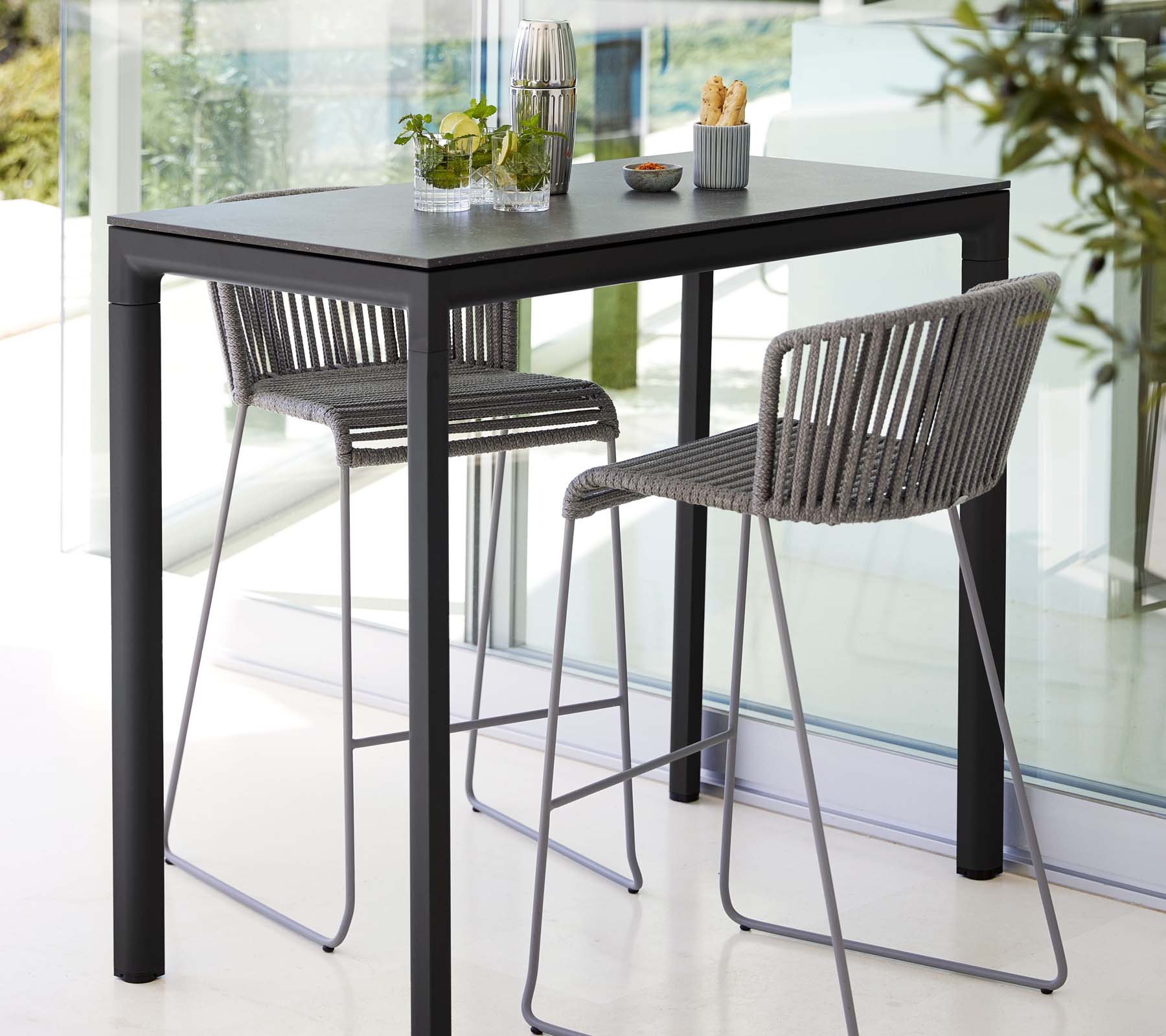 Modernes Tisch mit zwei stilvollen Hockern, die ein schlankes Design aufweisen, kombiniert mit dekorativen Pflanzen und minimalistischen Esszubehör.