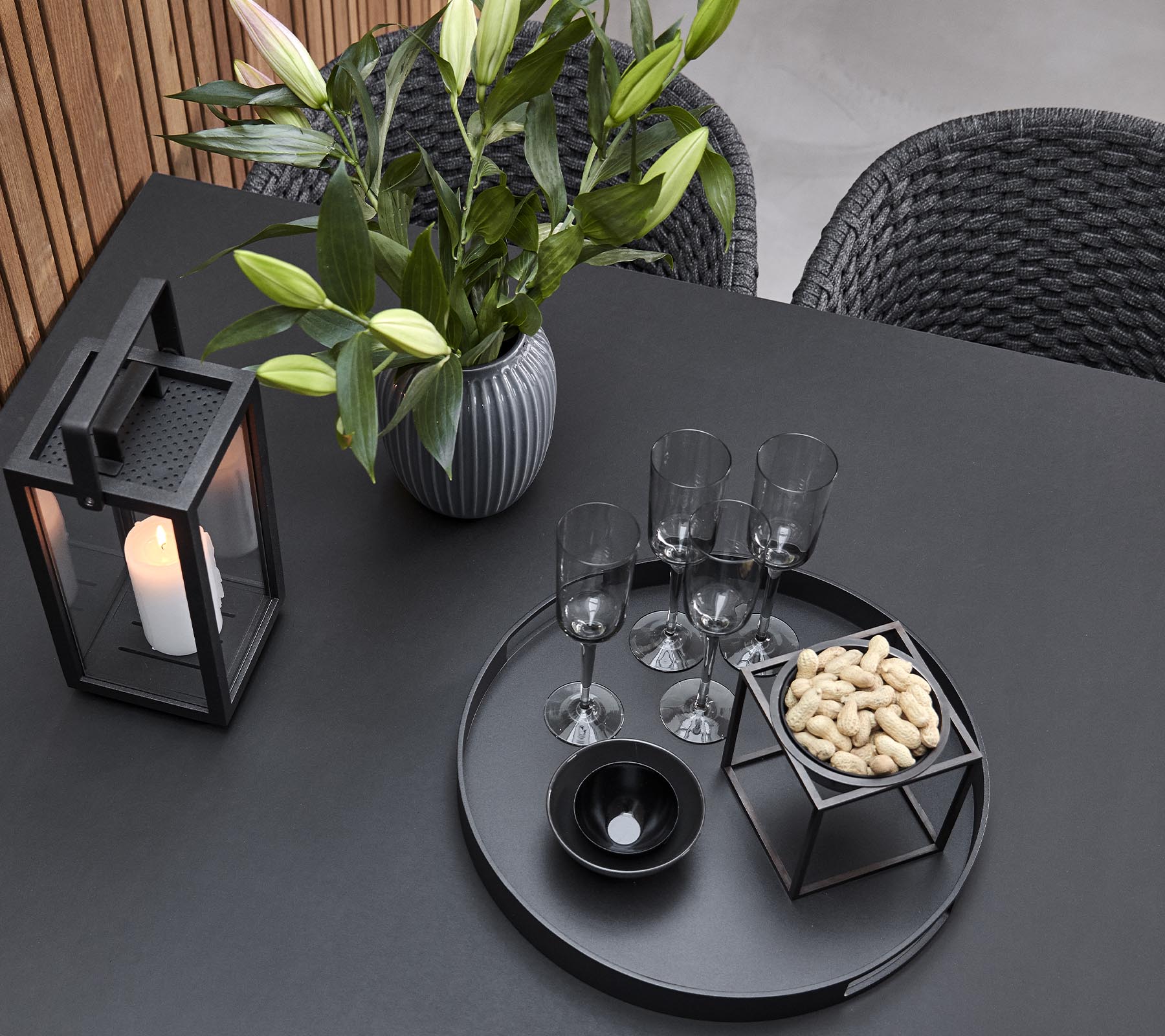 Ein stilvolles Tischarrangement mit einer Laterne, einer Vase mit Blumen, Gläsern und einem Serviertablett mit Snacks.