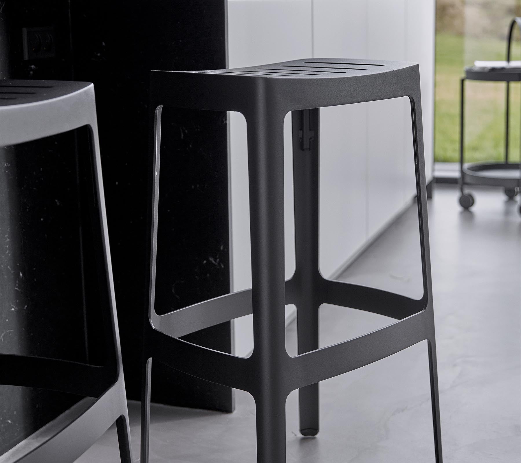 Ein schlanker, moderner Barhocker mit minimalistischen Design, der eine robuste Struktur und eine elegante schwarze Oberfläche aufweist.