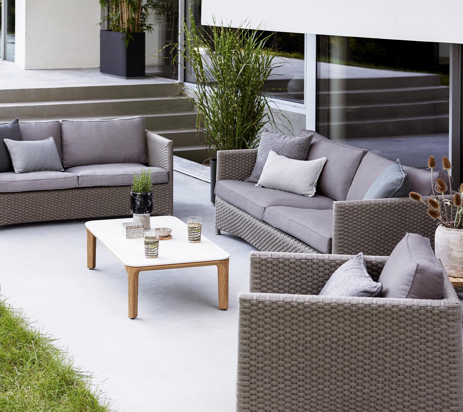 Zeitgemäße Außensitzgruppe mit einer 2-Sitzer-Sofa, einem 3-Sitzer-Sofa, Lounge-Stühlen und einem Couchtisch mit dekorativen Objekten.
