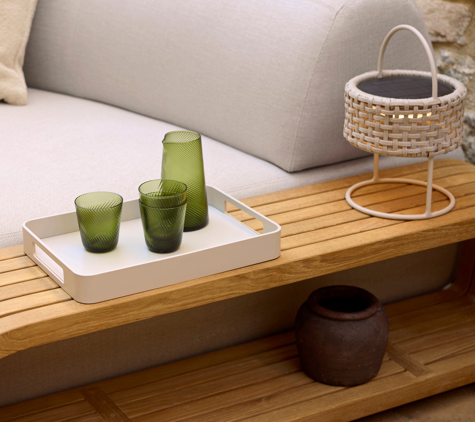 Ein gemütlicher Couchtisch mit einem weißen Tablett, drei grünen Gläsern, einer geflochtenen Lampe und einem dekorativen Topf, der eine ruhige Atmosphäre verleiht.