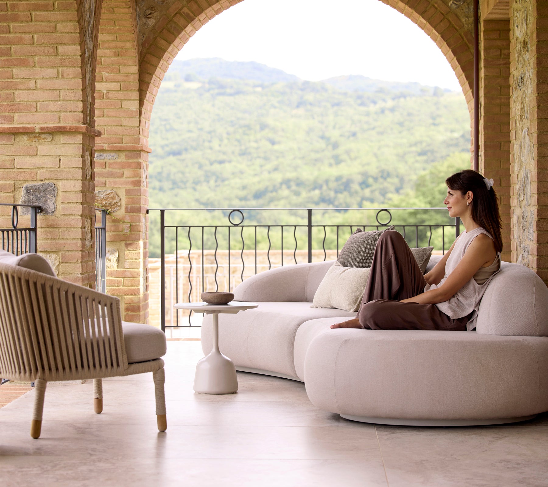 Ein ruhiger Sitzbereich mit einem sanften Lounge-Sofa, einem Moments-Lounge-Stuhl und einem Glaze-Couchtisch, umgeben von üppigem Grün im Hintergrund.