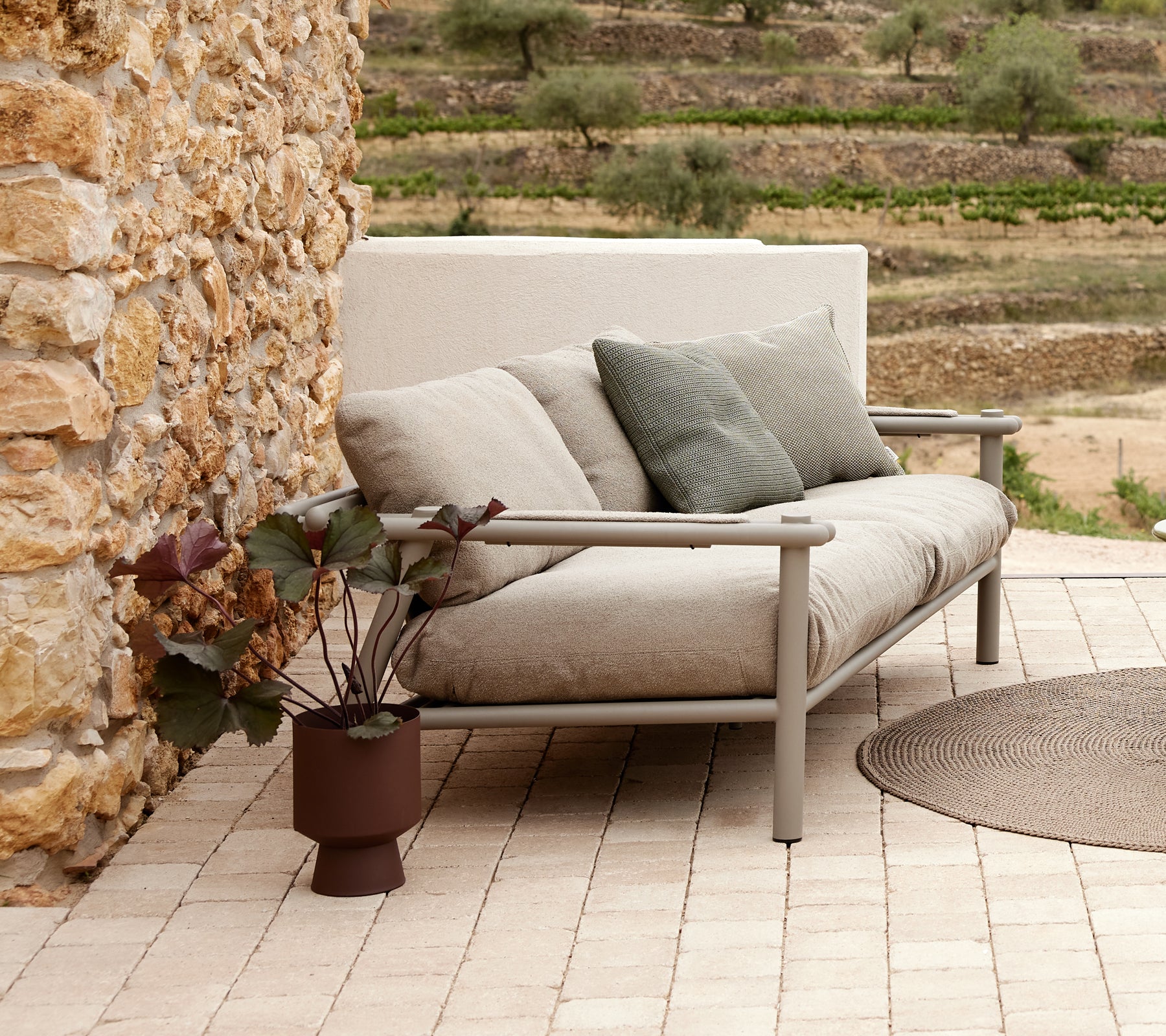 Ein modernes Sofa mit weichen Kissen und einem Aluminiumrahmen, begleitet von einer Topfpflanze auf einer gemusterten Fliese.