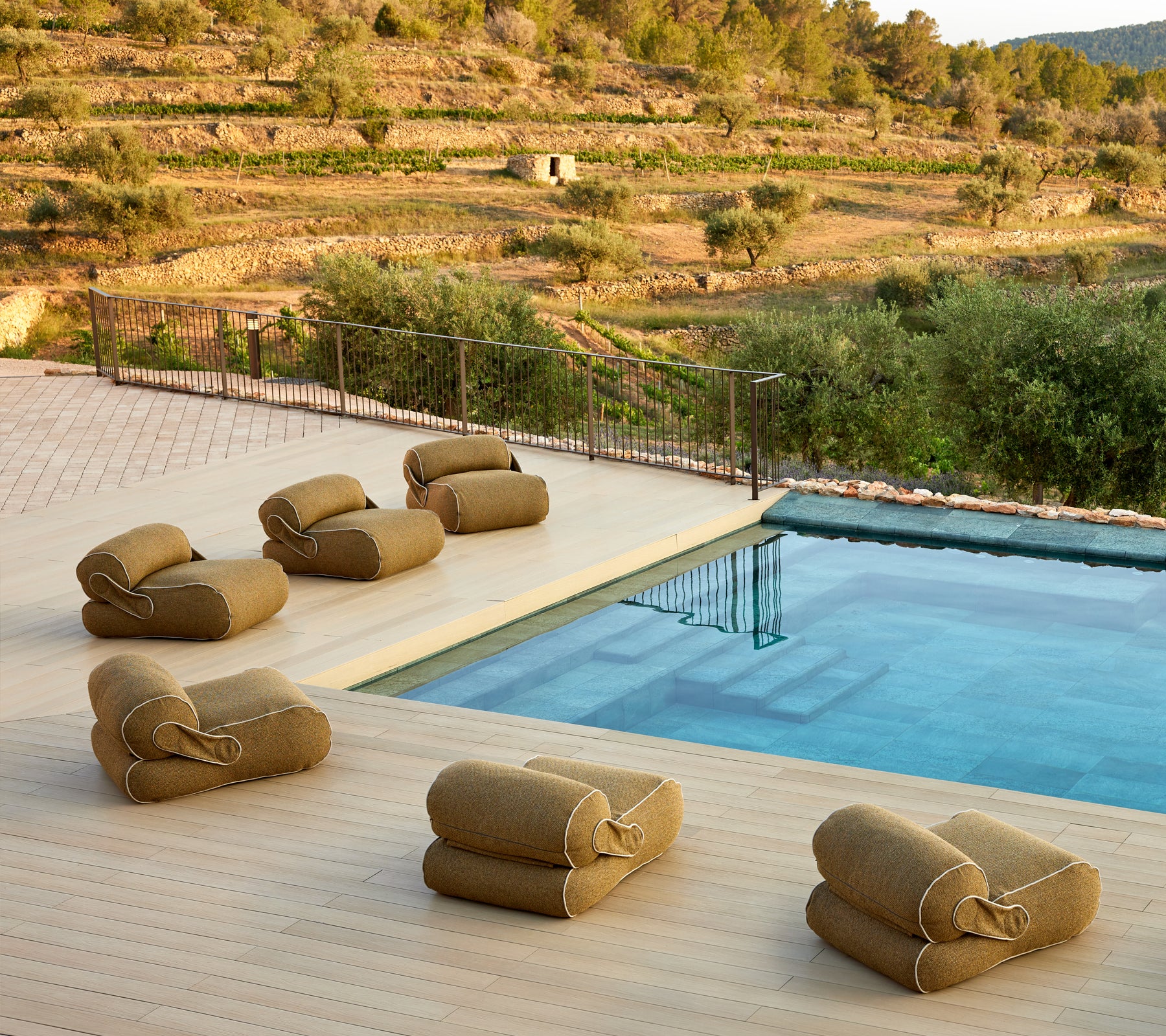 Eine ruhige Umgebung mit gepolsterten Loungemöbeln, die in der Nähe eines ruhigen Pools angeordnet sind, umgeben von üppigem Grün und einer malerischen Landschaft.
