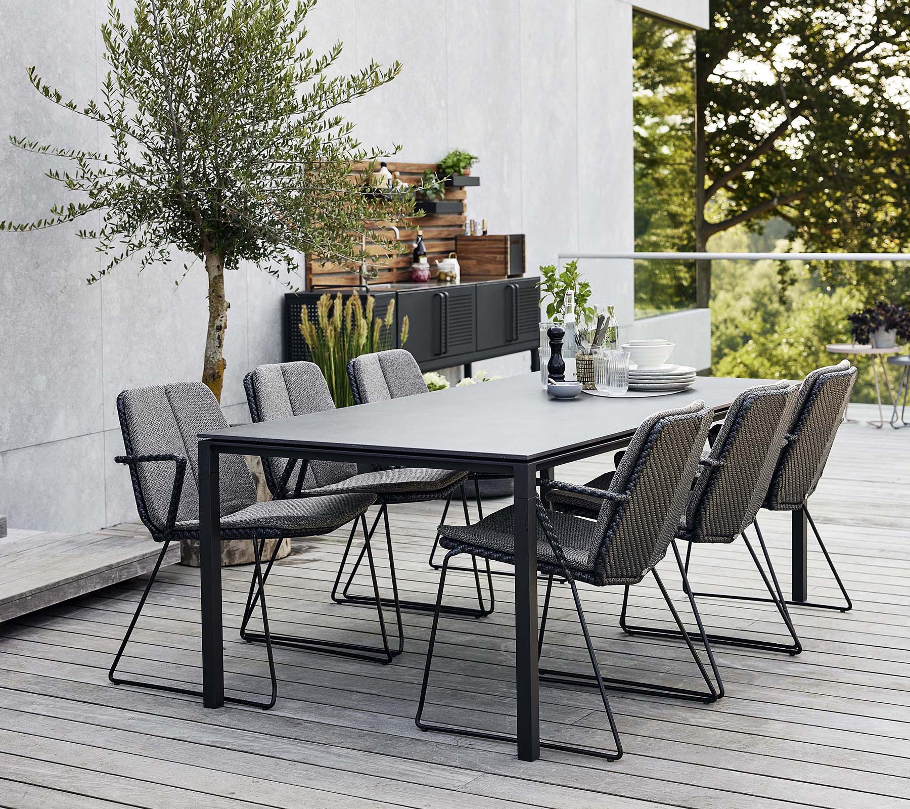 Ein stilvolles Garten-Esszimmer mit einem eleganten Tisch und mehreren bequemen Armlehnstühlen, umgeben von Grün und einem modernen Hintergrund.