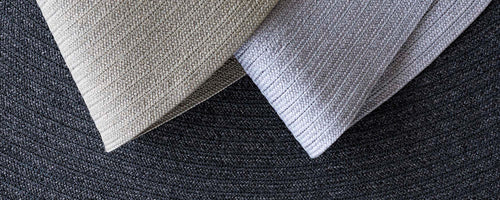 Zwei strukturierte Teppichmuster in hellen Farben, die kontrastierende Muster vor einem dunkleren Hintergrund zeigen.