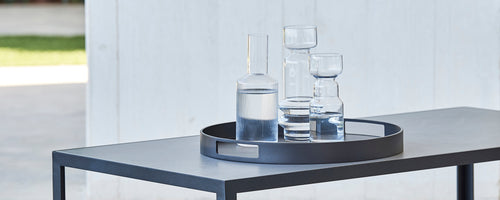Ein rundes Serviertablett mit verschiedenen Gläsern, darunter ein großer Krug und mehrere Gläser, auf einem eleganten Tisch platziert.