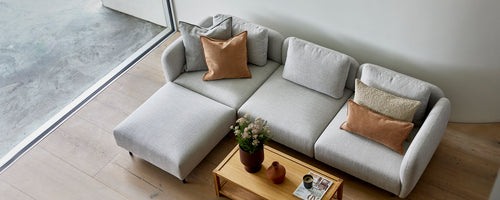 Ein stilvolles hellgraues Sofa mit gemütlichen Kissen, ergänzt durch einen Holztisch und eine kleine Topfpflanze.