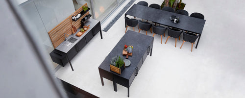 Aerial view of sleek dark tables and a sideboard, arranged with decorative plants and serving items.
