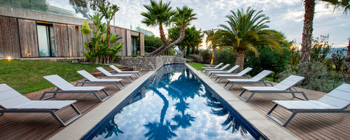 Eine Reihe von Liegen neben einem reflektierenden Pool, umgeben von üppigem Grün und Palmen, die einen ruhigen Entspannungsbereich schaffen.