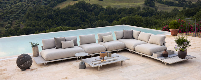 Eine stilvolle Anordnung von modularen Sofas mit Kissen, begleitet von einem Couchtisch und Pflanzen, vor einer malerischen Naturlandschaft.