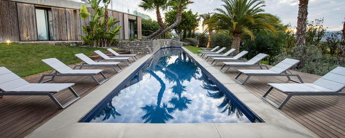 Eine ruhige Poollandschaft mit einer Reihe weißer Liegen neben einem ruhigen Wasser, umgeben von üppigem Grün und Palmen.