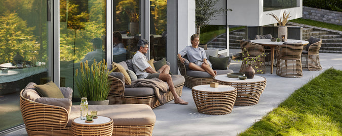 Moderne Rattanstühle mit grauen Kissen und einem Couchtisch in einem zeitgenössischen Außenlounge-Setting.