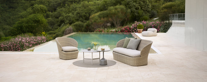 Modernes graues Sofa mit Kissen und rundem Tisch am Pool.