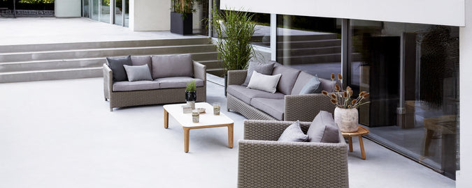 Moderne Outdoor-Lounge-Setup mit grauem Sofa, Sessel und weißem Tisch.