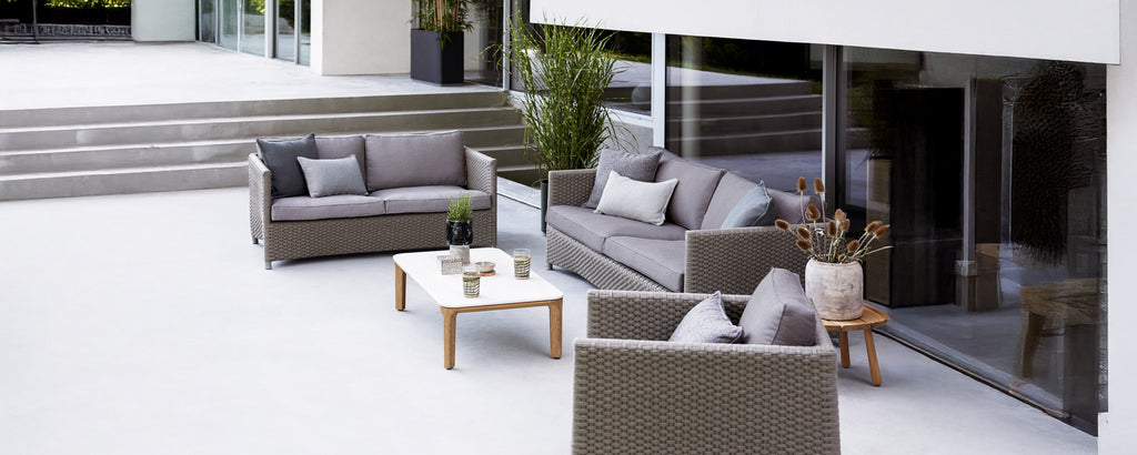 Moderne Outdoor-Lounge-Setup mit grauem Sofa, Sessel und weißem Tisch.