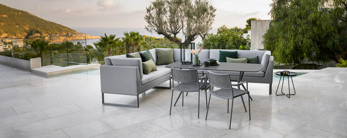 Moderne Außenloungebereich mit grauem Sofa, grünen Kissen, schwarzem Tisch und grauen Stühlen.