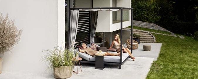 Moderne Außenloungebereich mit einem schwarzen Tagesbett, grauen Kissen und weißen Vorhängen.