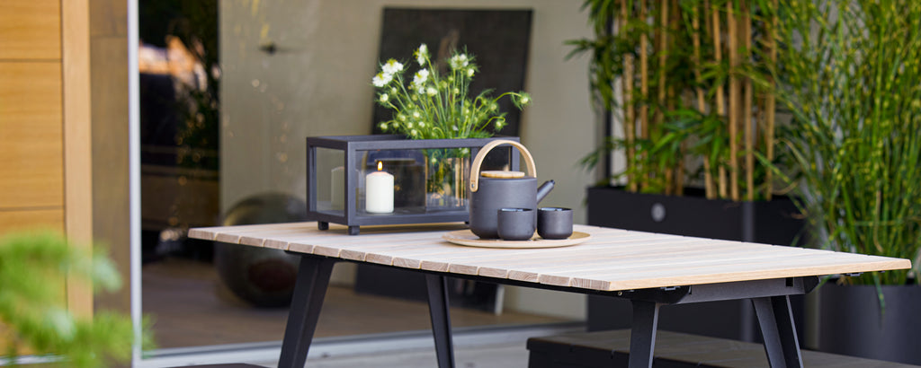Modernes Tisch mit schwarzem Laterne, Teekanne und Tasse, umgeben von Grün.